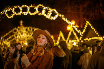 Christmas, New Year, winter holidays conception: happy smiling woman posing at night street festive fair, holding sparkler. Copy, empty space for text