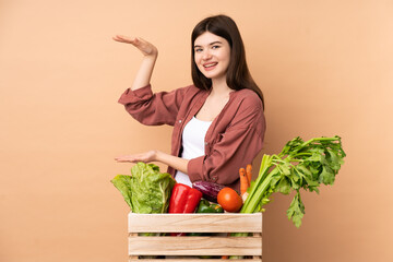 Young farmer girl with freshly picked vegetables in a box holding copyspace to insert an ad