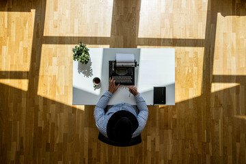 Top view shot of an author wearing a hat and typing typewriter with floating sun