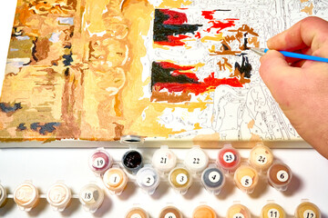 Man holding a brush and paints a picture, drawing by numbers.