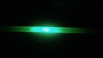 Bright green horizontal tube on a black background.
The transparent plastic tube is filled with a green glowing liquid. Green liquid glows in the dark. A chemical reaction is in progress. The liquid i