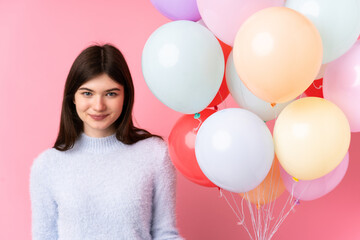 Fototapeta na wymiar Young Ukrainian teenager girl holding lots of balloons over isolated pink background