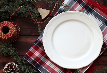 Fototapeta na wymiar Tavolino natalizio con piatto bianco vuoto e decorazioni natalizie. Sfondo di legno. Vista dall'alto. 