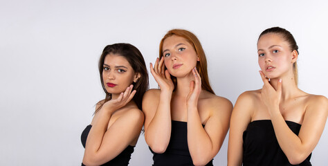 Three beautiful girls in black bodysuits posing on a white background in the studio. Spa and beauty concept