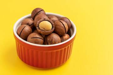 Macadamia nuts in a red bowl on yellow background.