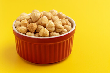 Hazelnut kernels in a red bowl. Peeled hazelnut on yellow background.