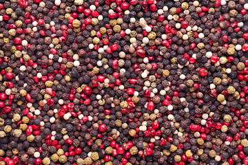Surface covered with multiple red, black and green pepper seeds as a background texture composition