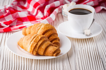 delicious fresh croissant and cup of coffee on a white wooden rustic background