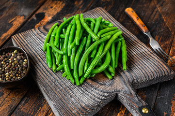Fresh green beans on a cutting board. Dark wooden background. top view