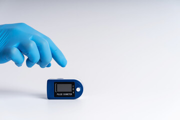 Pulse oximeter on a white background. A hand in a medical glove holds a device for health diagnostics