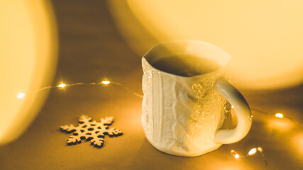 Unique ceramic tea cup with knit pattern with a wooden snowflake decoration with warm Christmas lights and bokeh defocused effect