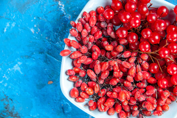 top half view currants and barberries in white plate on blue background free space