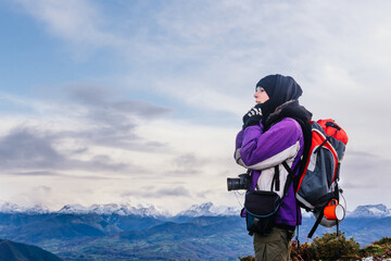 Warmly bundled nature photographer with backpack taking a breather while ascending a mountain....