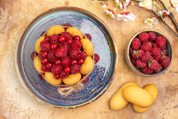 Overhead view of freshly baked soft cake with fruits and biscuits on mixed color table