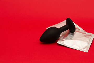Silicone butt plug and condoms. Adult toys on red background with copy space