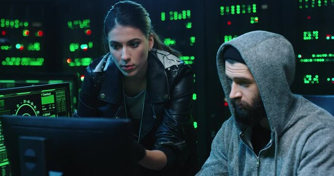 Close up of couple of hackers man and woman monitoring database hacking operation while browsing computer. Cybercrime.