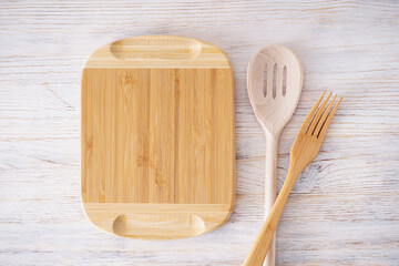 Wooden cutting board and kitchenware on wooden background, space for text, flat lay.