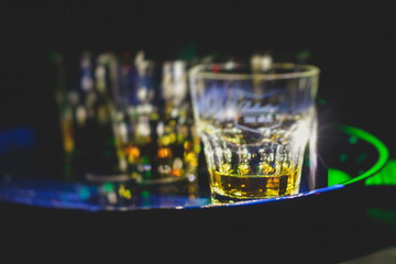 Beautiful row of different colored alcohol cocktails on a party, whiskey, scotch whisky, and others, glasses on a bar counter, bar stand, with bartender in the background
