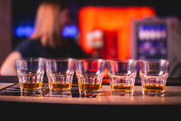 Beautiful row of different colored alcohol cocktails on a party, whiskey, scotch whisky, and others, glasses on a bar counter, bar stand, with bartender in the background