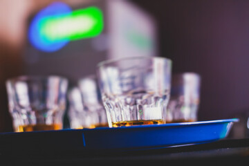 Beautiful row of different colored alcohol cocktails on a party, whiskey, scotch whisky, and others, glasses on a bar counter, bar stand, with bartender in the background