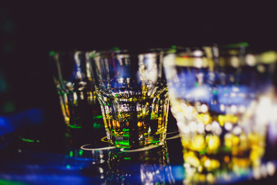 Beautiful row of different colored alcohol cocktails on a party, whiskey, scotch whisky, and others, glasses on a bar counter, bar stand, with bartender in the background