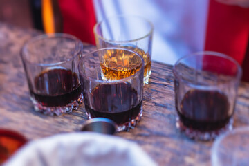 Beautiful row of different colored alcohol cocktails on a party, whiskey, scotch whisky, and others, glasses on a bar counter, bar stand, with bartender in the background