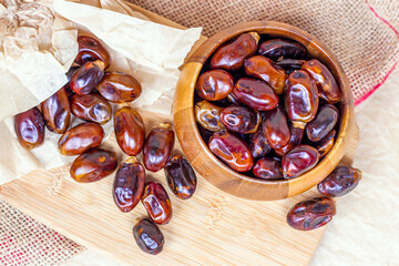 Sweet dried dates in round wooden bowl on light background in the kitchen.