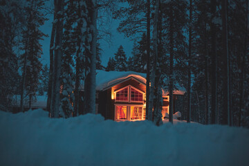 A night view of cozy wooden scandinavian cabin cottage chalet house covered in snow near ski resort...