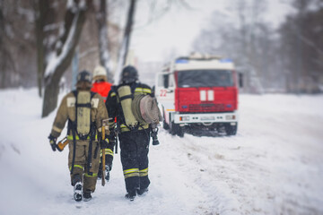 Group of fire men in uniform, firefighters with the fire engine truck fighting vehicle in the background, winter streets