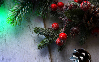 Fir tree snow covered branches with shiny holly berries and cones on wooden background. Green led...