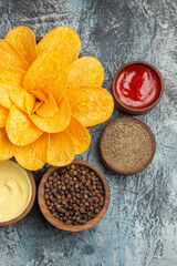 Vertical view of homemade potato chips decorated like flower shaped different spices and ketchup on gray background