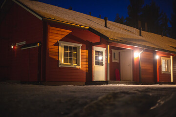 A view of cozy wooden scandinavian cabin cottage chalet house covered in snow near ski resort in winter with the lights on, evening picture