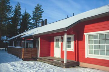A view of cozy wooden scandinavian cabin cottage chalet house covered in snow near ski resort in winter with the lights on, evening picture