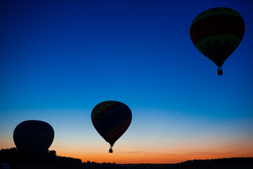 Three Colorful Air Balloons Levitating Over the Field Outdoors Against Clear Blue Skies At Twilight.