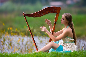Portrait of Dreaming Sensual Female Harpist in Light Dress Playing Music Outdoor in Park.