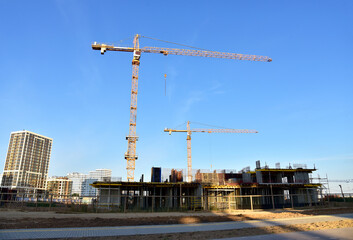 Fototapeta na wymiar Tower cranes working at construction site on blue sky background. Construction process of the new modern residential buildings
