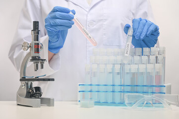 Macro shot view of microbiologist in protective blue gloves holds biological tubes with covid-19 vaccine on laboratory background. Backstage of scientific discovery. Healthcare and medicine concept.