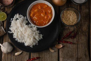 Top view of plate with delicious chicken tikka masala curry and rice on rustic wooden table with spices background. Traditional Indian dish. Exotic tasty meal. Appetizing photo for cookbook.