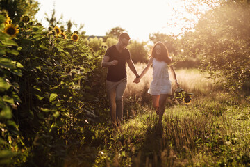 Beautiful couple having fun in sunflowers field. A man and a woman in love walk in a field with sunflowers, a man hugs a woman. selective focus