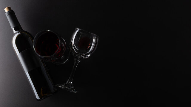 Elegant dark bottle and glasses with remains of red wine on rustic black background. Advertising and promotion concept. Mock up. Flat lay. View from above. Space for text.