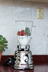 blender with milk, spinach and strawberries on a kitchen counter