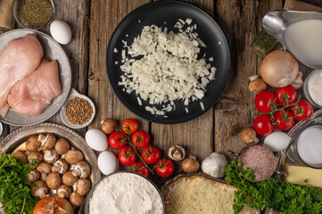 The plate with chopped onion for preparing filling on wooden table with variety of ingredients background. Concept of cooking process. Backstage of preparing pie. View from above.