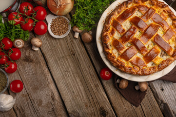 Ruddy pie with meat and mushrooms on wooden table with variety of ingredients background. Cooking process. Backstage of preparing tasty meal. View from above. Flat lay. Recipe book. Space for text.