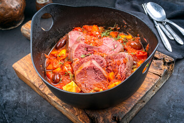 Modern style traditional Peruvian estofado de lengua cooked beef tongue with vegetable and olives as stew as close-up in a design pot