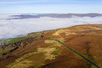 Aerial view of a narrow, winding mountain road on a hillside above a fog filled valley