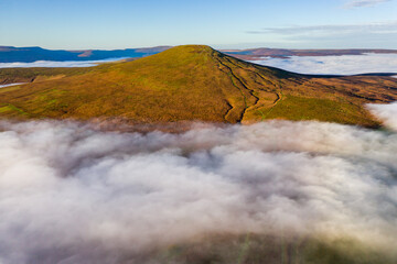 Aerial view of a mountain peak rising above a sea of low cloud and fog in the valley below (Sugar Loaf, Wales)
