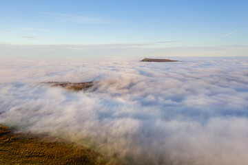 Aerial view of mountains rising above a sea of fog on a bright, sunny day