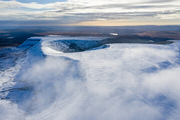 Aerial drone view of snow covered mountains and ridges rising above a brown valley (Neuadd, Wales)