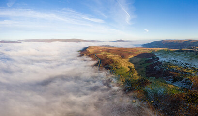 Aerial panorama of a narrow, winding mountain road emerging above a bank of fog in a rural valley