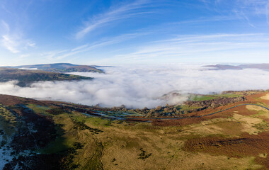 Aerial panorama of a narrow, winding mountain road emerging above a bank of fog in a rural valley